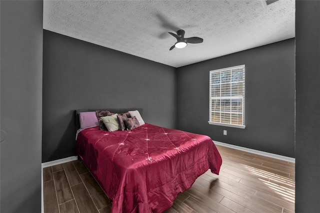 bedroom with a ceiling fan, wood tiled floor, a textured ceiling, and baseboards