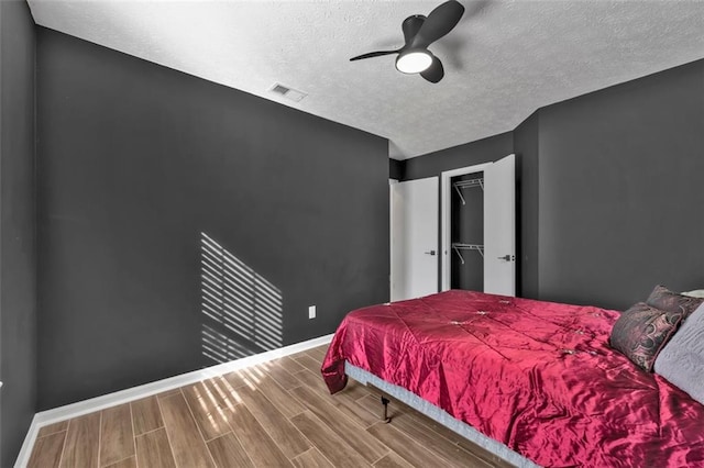 bedroom featuring visible vents, baseboards, a ceiling fan, wood tiled floor, and a textured ceiling