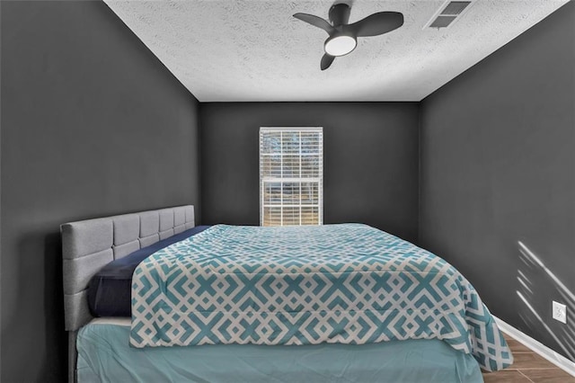 bedroom with a textured ceiling, ceiling fan, wood finished floors, visible vents, and baseboards