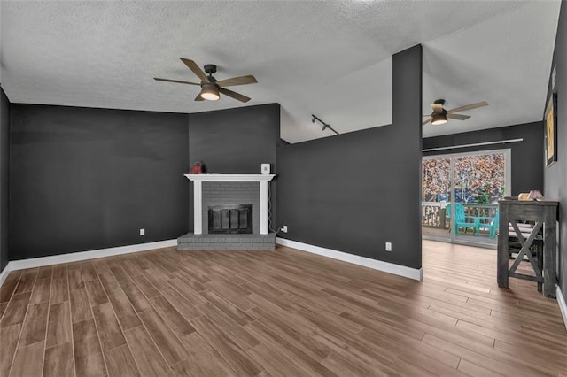 unfurnished living room with baseboards, ceiling fan, wood finished floors, a textured ceiling, and a fireplace