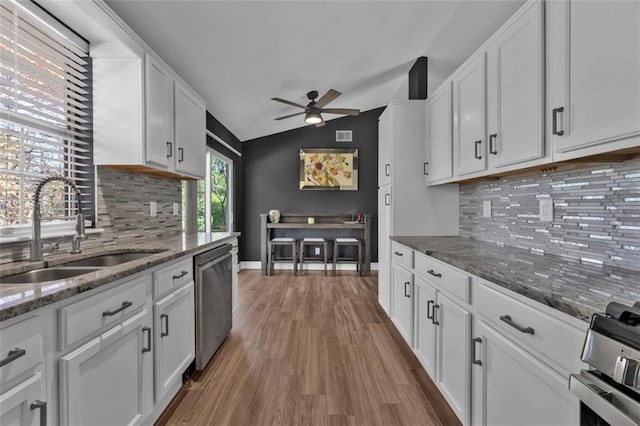 kitchen with lofted ceiling, white cabinets, stainless steel appliances, and a sink