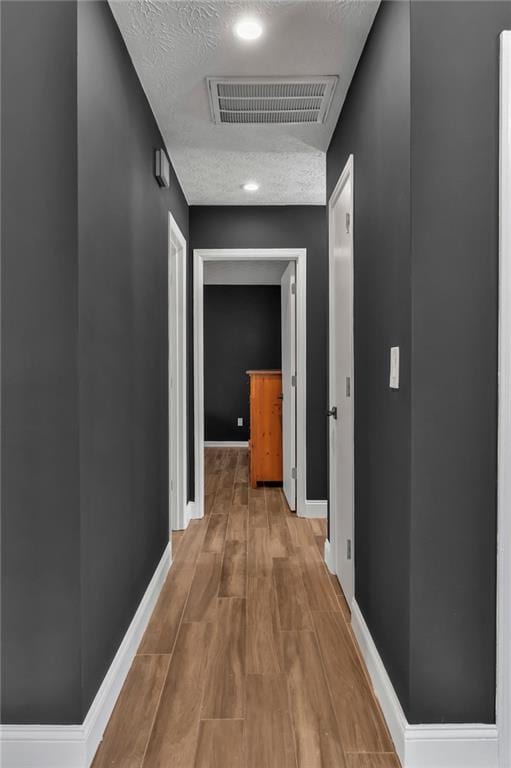 hall featuring light wood-style floors, baseboards, visible vents, and a textured ceiling