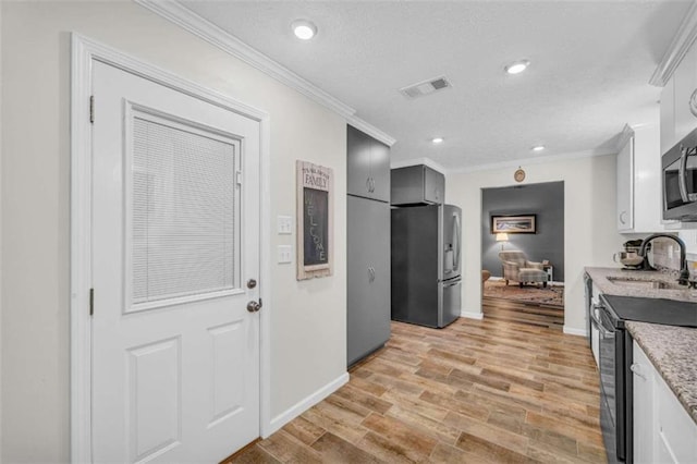 kitchen with white cabinetry, sink, stainless steel appliances, light wood-type flooring, and ornamental molding