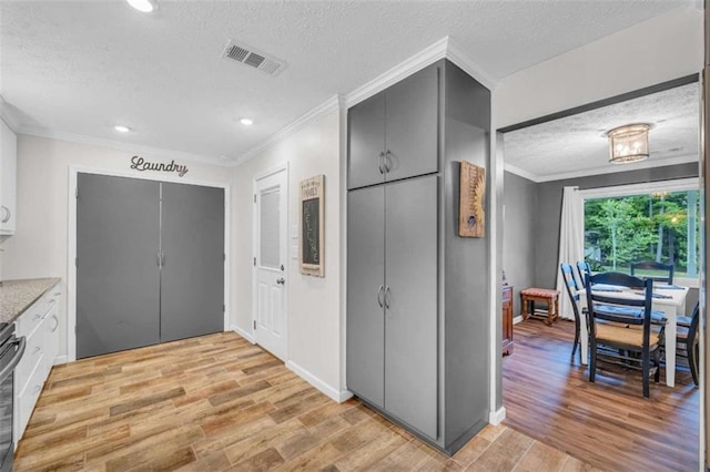 kitchen with white cabinets, crown molding, stainless steel stove, a textured ceiling, and light hardwood / wood-style floors