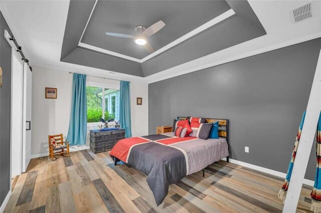 bedroom with crown molding, ceiling fan, a barn door, a tray ceiling, and wood-type flooring