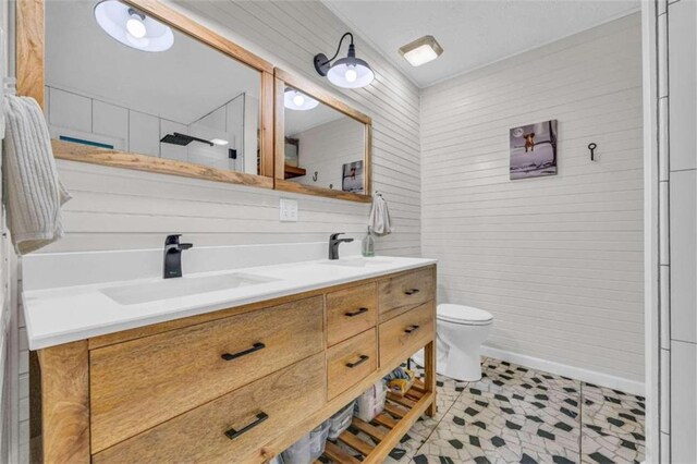 bathroom with tile patterned floors, wooden walls, vanity, and toilet