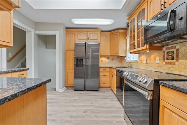 kitchen featuring dark stone countertops, light hardwood / wood-style floors, black appliances, decorative backsplash, and sink