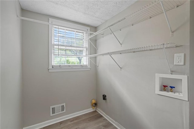 clothes washing area with a textured ceiling, hardwood / wood-style flooring, and hookup for a washing machine