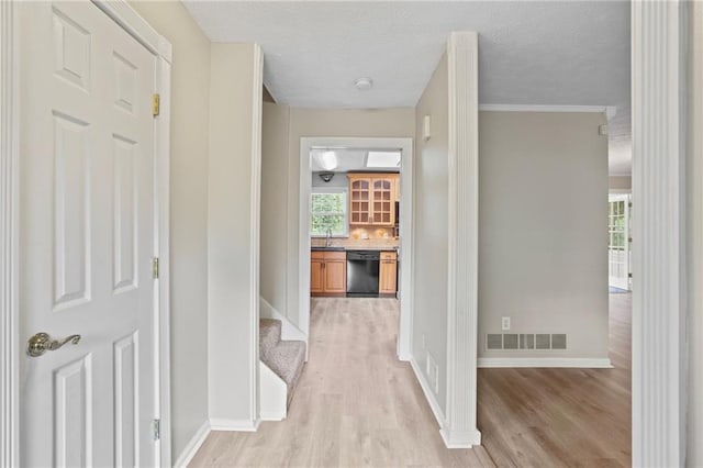 hallway with sink, crown molding, a textured ceiling, and light hardwood / wood-style flooring