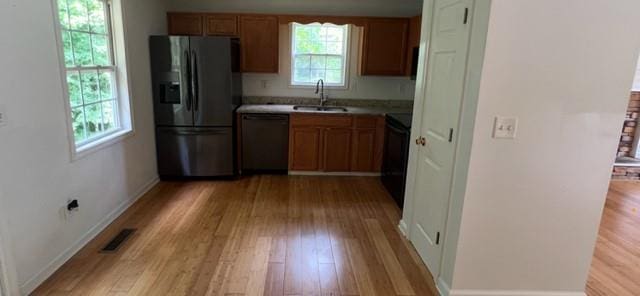 kitchen featuring stainless steel fridge with ice dispenser, dishwashing machine, a sink, and light wood-style floors