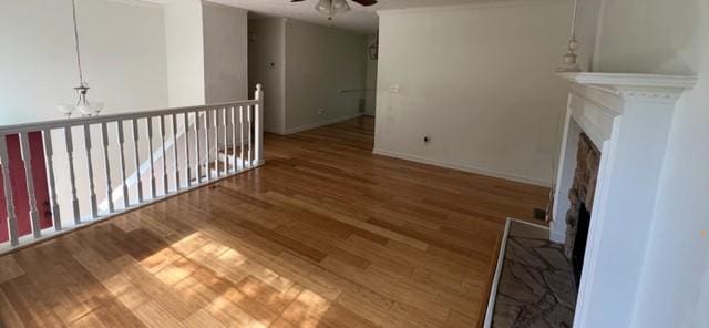unfurnished living room with a fireplace with raised hearth, a ceiling fan, wood finished floors, a chandelier, and baseboards