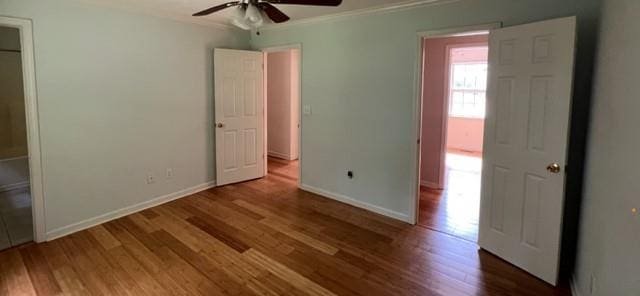 unfurnished bedroom with ornamental molding, wood finished floors, baseboards, and ceiling fan
