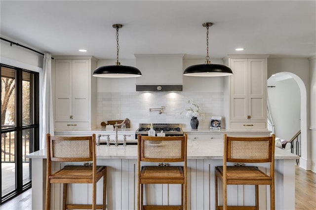 kitchen featuring tasteful backsplash, hanging light fixtures, light wood-type flooring, and a kitchen bar