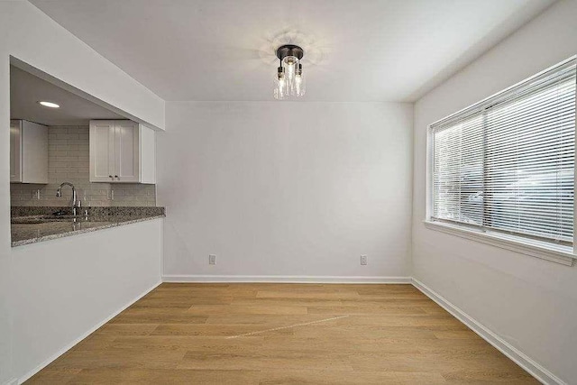 unfurnished dining area with light wood finished floors, baseboards, and a sink