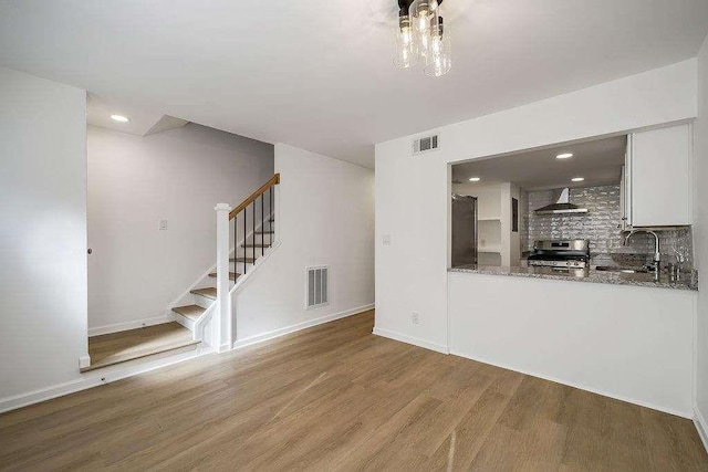 unfurnished living room featuring a sink, wood finished floors, visible vents, stairs, and baseboards