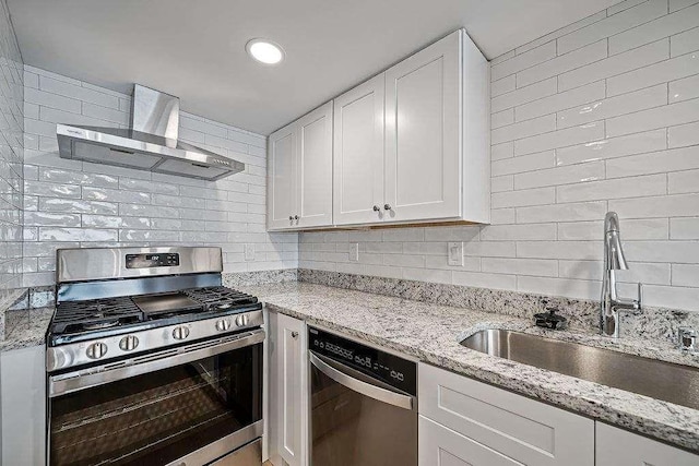 kitchen with decorative backsplash, appliances with stainless steel finishes, white cabinets, a sink, and wall chimney range hood