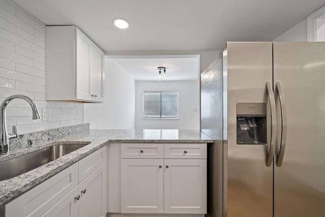 kitchen featuring light stone counters, a sink, white cabinetry, backsplash, and stainless steel fridge