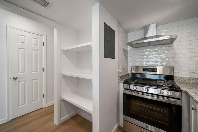 kitchen with tasteful backsplash, light wood-style floors, wall chimney range hood, electric panel, and stainless steel gas range oven