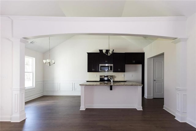 kitchen featuring appliances with stainless steel finishes, a kitchen island with sink, hanging light fixtures, decorative columns, and a notable chandelier