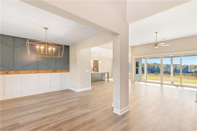 spare room with ceiling fan with notable chandelier and light wood-type flooring