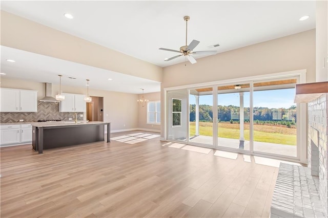 unfurnished living room featuring sink, light hardwood / wood-style floors, and ceiling fan with notable chandelier