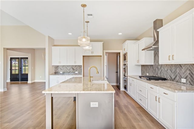 kitchen with a center island with sink, light wood-type flooring, white cabinetry, and hanging light fixtures