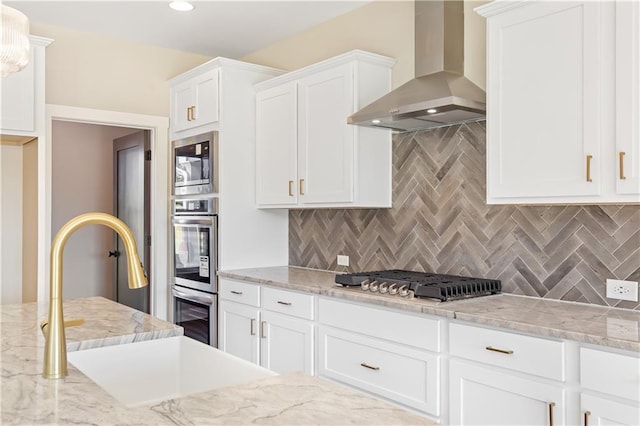 kitchen with tasteful backsplash, white cabinets, wall chimney exhaust hood, and appliances with stainless steel finishes