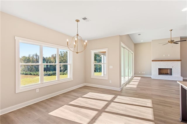 unfurnished dining area featuring light hardwood / wood-style floors, ceiling fan with notable chandelier, and a brick fireplace