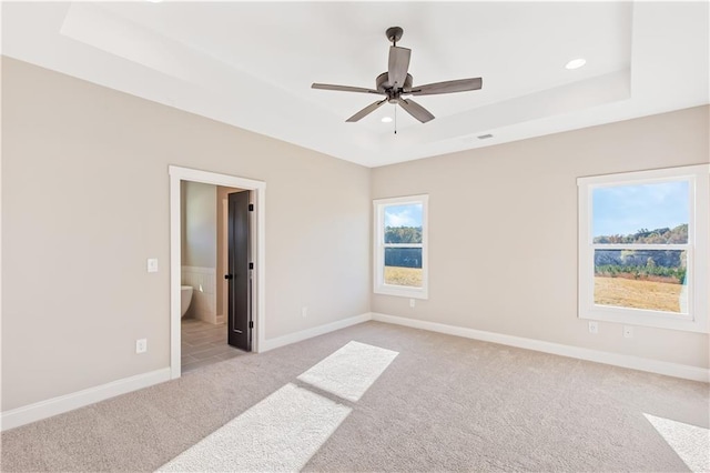 carpeted spare room with a raised ceiling and ceiling fan