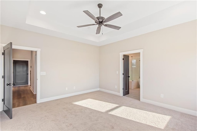 unfurnished bedroom with a raised ceiling, ensuite bath, ceiling fan, and light colored carpet