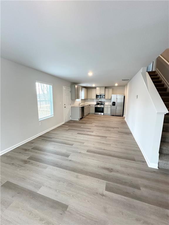 unfurnished living room featuring stairs, light wood-type flooring, recessed lighting, and baseboards