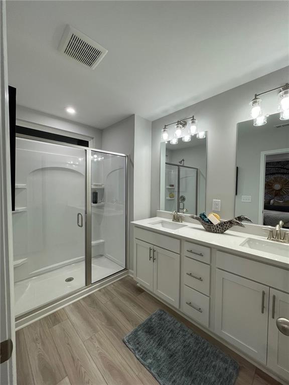 bathroom with visible vents, a sink, a shower stall, and wood finished floors