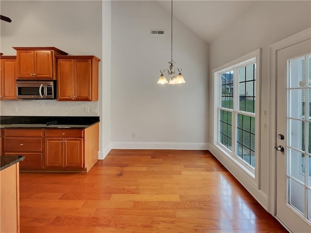 6405 Beaver Creek Trl, Atlanta, GA 30349 - kitchen with visible vents, light wood-style floors, high vaulted ceiling, stainless steel microwave, and a notable chandelier