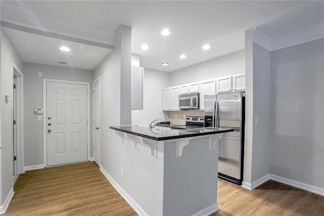 kitchen with stainless steel appliances, kitchen peninsula, a kitchen bar, decorative backsplash, and white cabinets