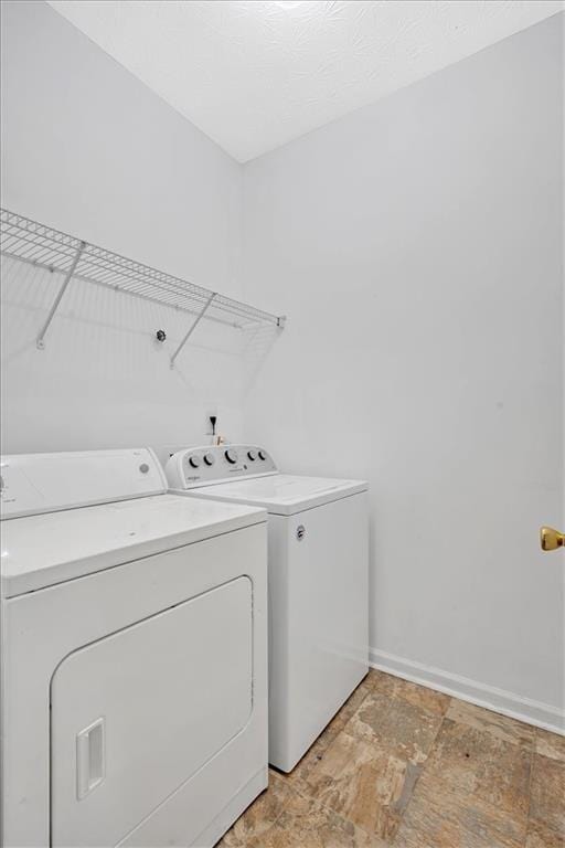 clothes washing area with laundry area, stone finish flooring, baseboards, and washing machine and clothes dryer