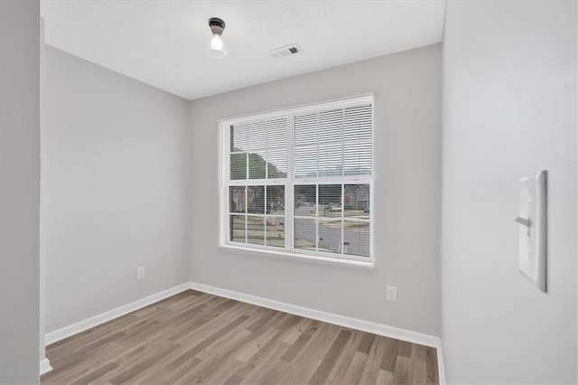 spare room with wood finished floors, visible vents, and baseboards