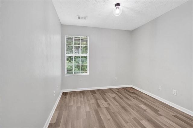 unfurnished room featuring visible vents, a textured ceiling, baseboards, and wood finished floors