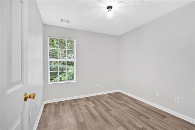 empty room featuring wood finished floors, visible vents, and baseboards