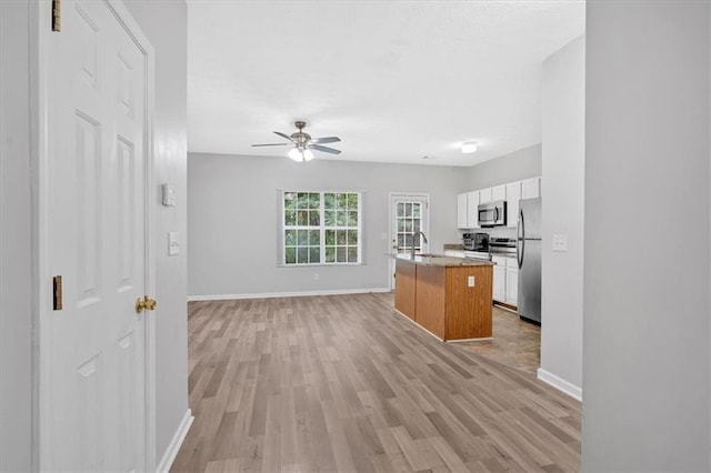 kitchen with a kitchen island with sink, a sink, white cabinetry, appliances with stainless steel finishes, and light wood finished floors