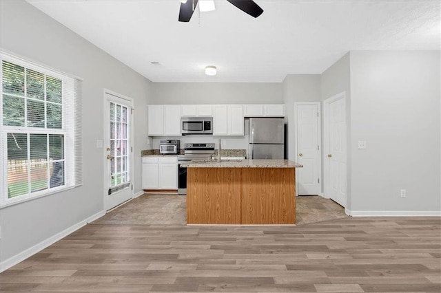 kitchen with appliances with stainless steel finishes, light wood-style floors, a kitchen island with sink, white cabinetry, and baseboards