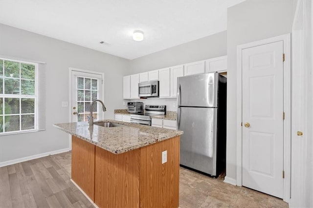 kitchen with an island with sink, appliances with stainless steel finishes, light stone countertops, white cabinetry, and a sink