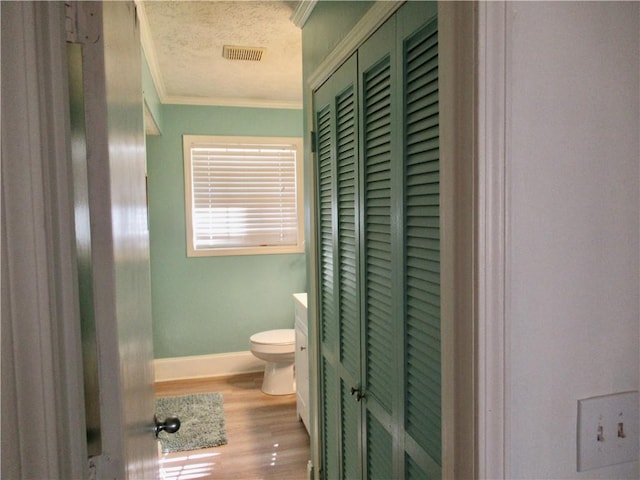 bathroom with crown molding, visible vents, toilet, a textured ceiling, and wood finished floors