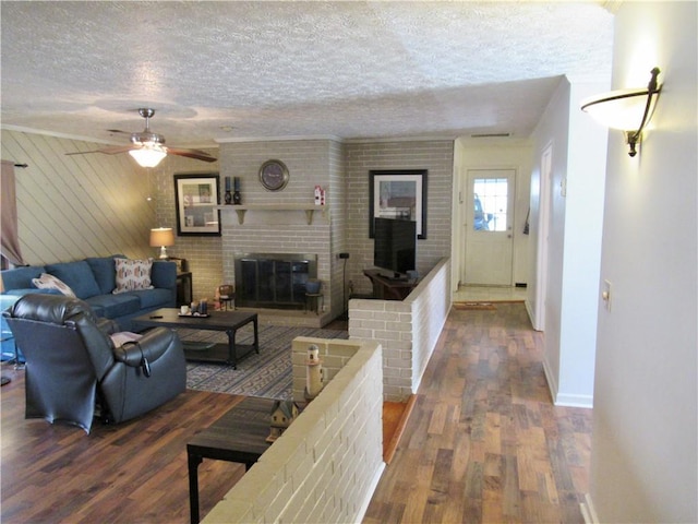 living area featuring a fireplace, ceiling fan, a textured ceiling, wood finished floors, and baseboards