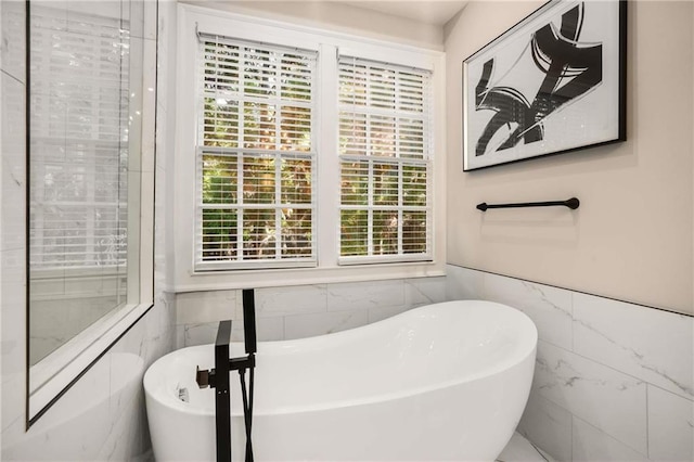 full bathroom featuring a freestanding tub, a wainscoted wall, and tile walls