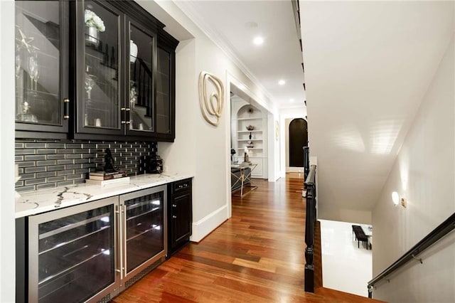 bar featuring arched walkways, wine cooler, ornamental molding, a dry bar, and dark wood finished floors