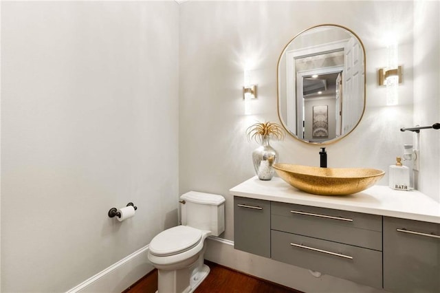 bathroom featuring toilet, baseboards, wood finished floors, and vanity