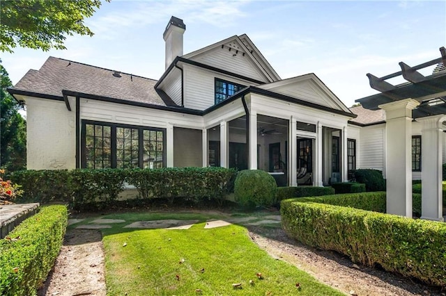 back of house featuring a sunroom, a lawn, and brick siding