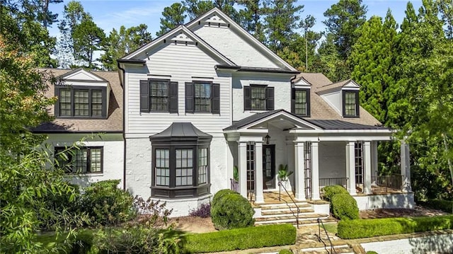 view of front of house featuring a standing seam roof, brick siding, metal roof, and covered porch