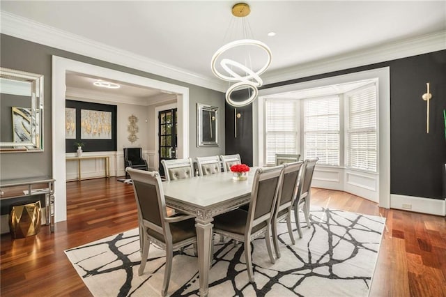 dining space with crown molding, a chandelier, a decorative wall, and wood finished floors