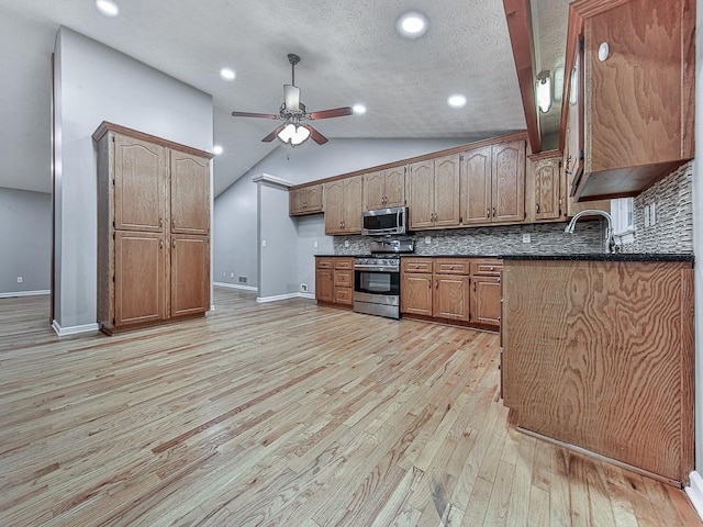 kitchen with vaulted ceiling, appliances with stainless steel finishes, backsplash, ceiling fan, and light hardwood / wood-style floors